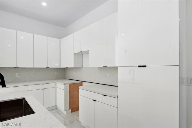 kitchen featuring light stone counters, white cabinetry, marble finish floor, backsplash, and modern cabinets