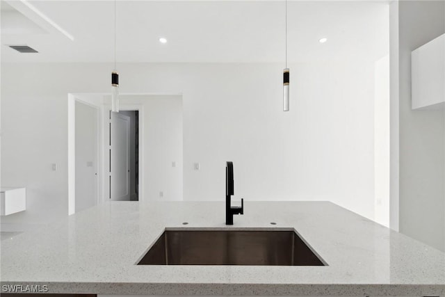 kitchen featuring light stone counters, visible vents, a sink, and hanging light fixtures