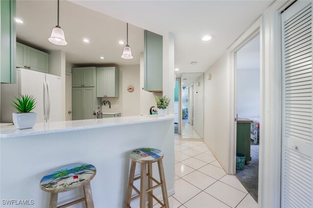 kitchen with white refrigerator, decorative light fixtures, green cabinets, and a breakfast bar area