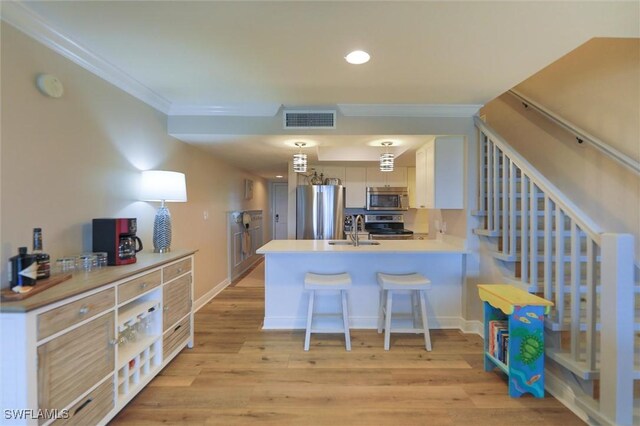 kitchen featuring stainless steel appliances, a kitchen bar, light wood-type flooring, kitchen peninsula, and hanging light fixtures