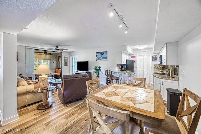 dining room with ceiling fan, light hardwood / wood-style flooring, a textured ceiling, and track lighting