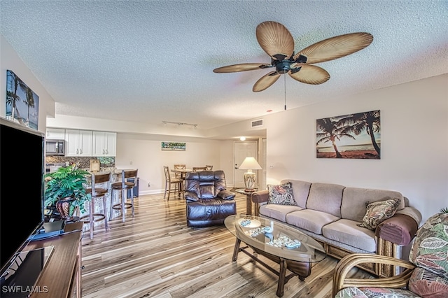 living room with a textured ceiling, visible vents, baseboards, a ceiling fan, and light wood-type flooring