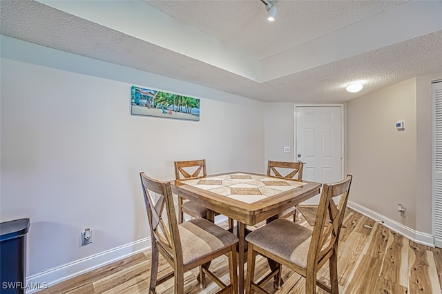 dining room featuring a textured ceiling, light hardwood / wood-style flooring, and track lighting