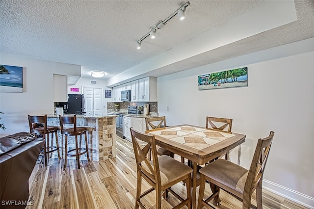 dining room featuring track lighting, a textured ceiling, and light hardwood / wood-style floors