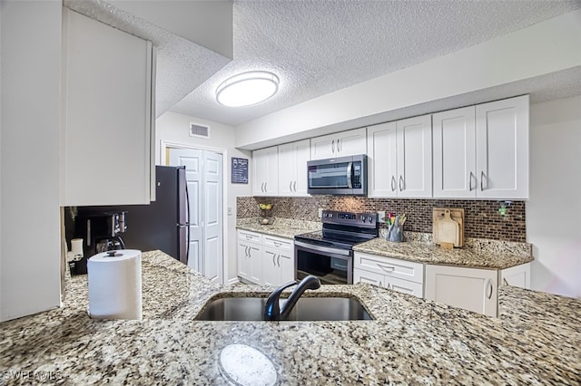 kitchen featuring light stone counters, appliances with stainless steel finishes, a sink, and white cabinetry