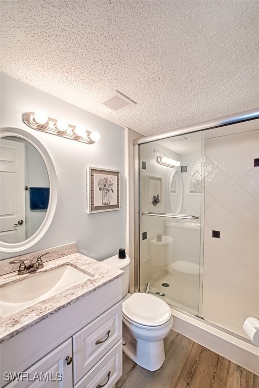 bathroom with hardwood / wood-style floors, vanity, a textured ceiling, toilet, and a shower with door