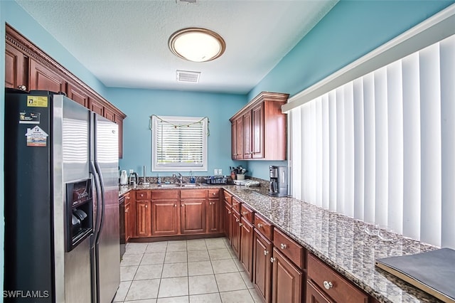 kitchen with sink, dishwashing machine, light tile patterned floors, stainless steel fridge, and dark stone countertops