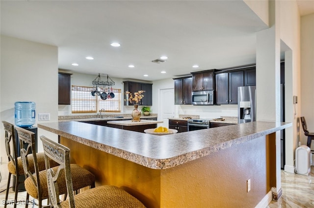 kitchen featuring dark brown cabinetry, appliances with stainless steel finishes, a kitchen breakfast bar, and a kitchen island