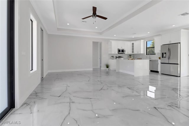 interior space with appliances with stainless steel finishes, tasteful backsplash, a kitchen island, light tile patterned floors, and a tray ceiling