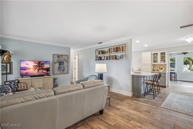 living room featuring ornamental molding, baseboards, visible vents, and light wood finished floors