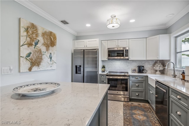 kitchen with light stone counters, a sink, appliances with stainless steel finishes, gray cabinets, and crown molding