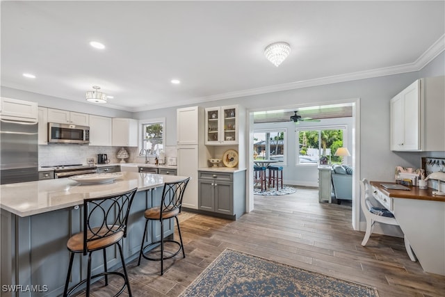 kitchen with crown molding, stainless steel appliances, backsplash, wood finished floors, and a kitchen bar