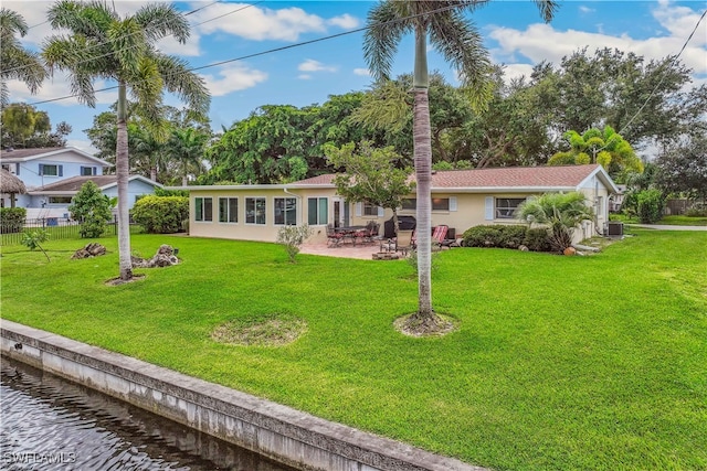 rear view of property featuring stucco siding, a water view, a lawn, a patio area, and fence