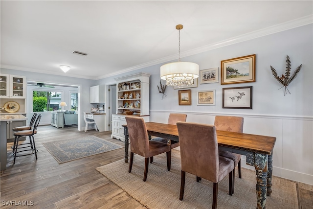 dining room with wainscoting, wood finished floors, visible vents, and crown molding