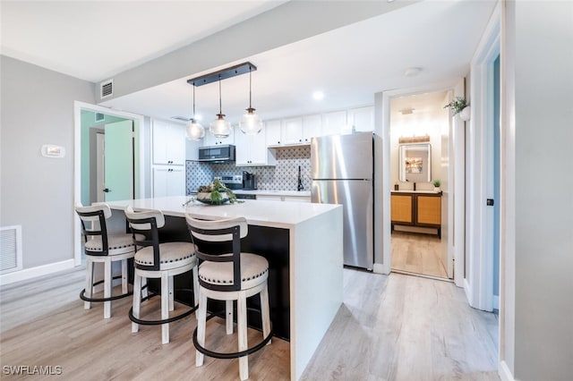 kitchen featuring white cabinetry, light hardwood / wood-style flooring, pendant lighting, a kitchen island, and appliances with stainless steel finishes