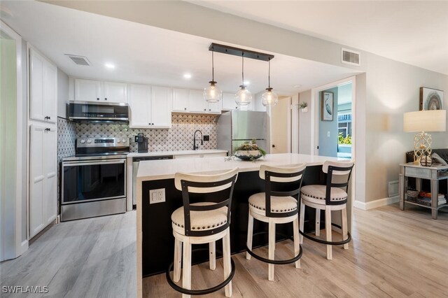 kitchen with white cabinets, decorative backsplash, light wood-type flooring, appliances with stainless steel finishes, and a kitchen island