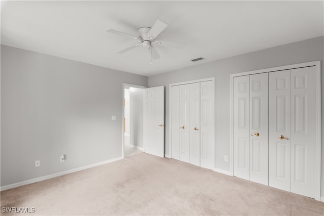 unfurnished bedroom with carpet flooring, ceiling fan, and multiple closets