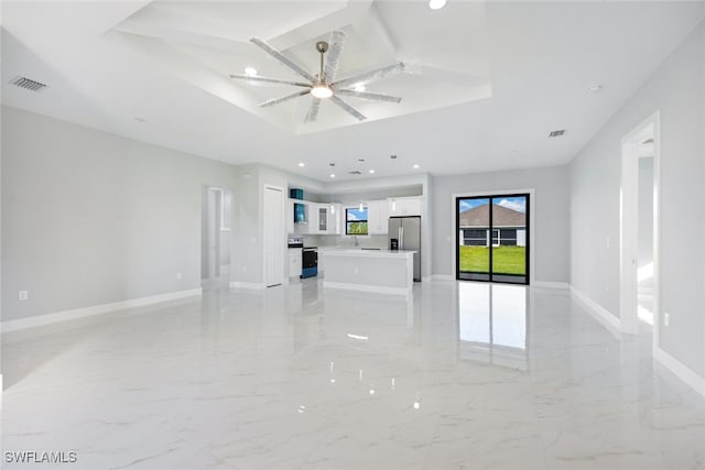 unfurnished living room featuring ceiling fan and a raised ceiling