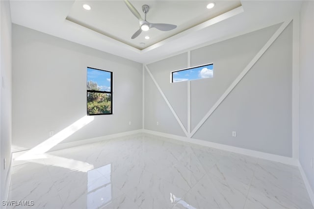 empty room with ceiling fan and a raised ceiling