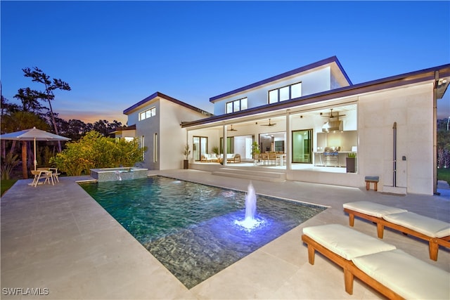 pool at dusk featuring an in ground hot tub, ceiling fan, and a patio area