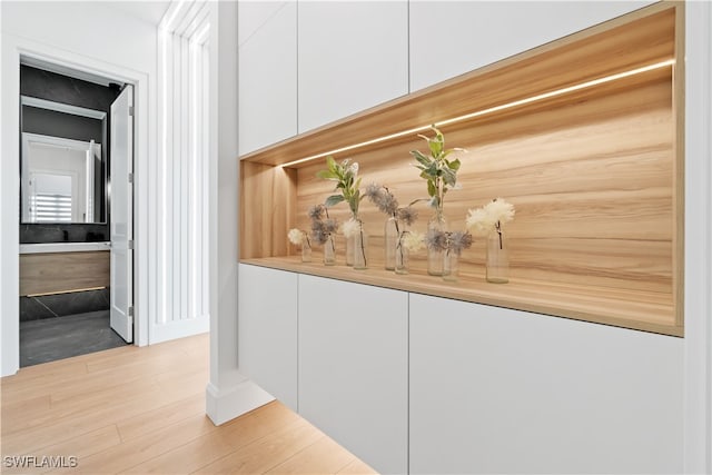 bar with light wood-type flooring and white cabinetry