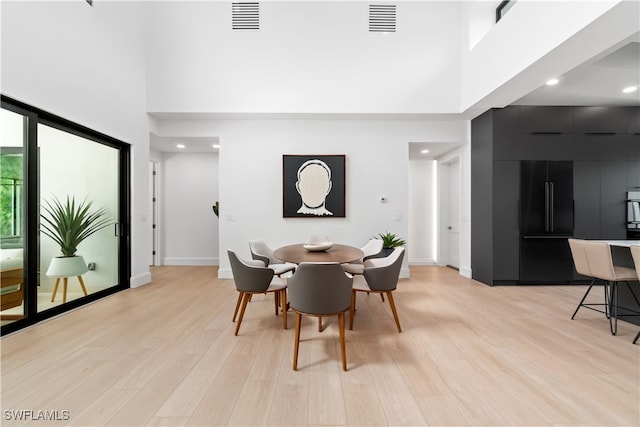 dining area with a towering ceiling and light hardwood / wood-style flooring