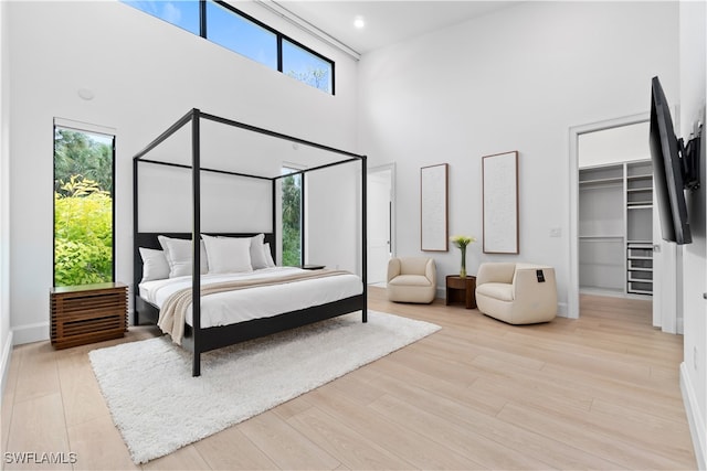 bedroom with a high ceiling, a walk in closet, light hardwood / wood-style flooring, and a closet