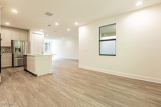 kitchen featuring backsplash, stainless steel fridge, a kitchen island with sink, and light wood-type flooring