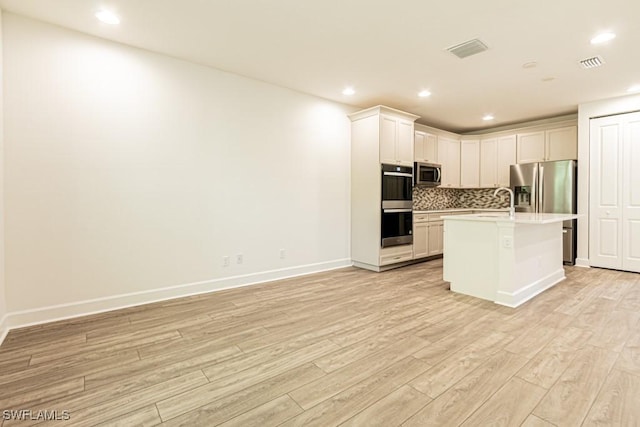 kitchen featuring decorative backsplash, stainless steel appliances, white cabinets, light hardwood / wood-style floors, and an island with sink