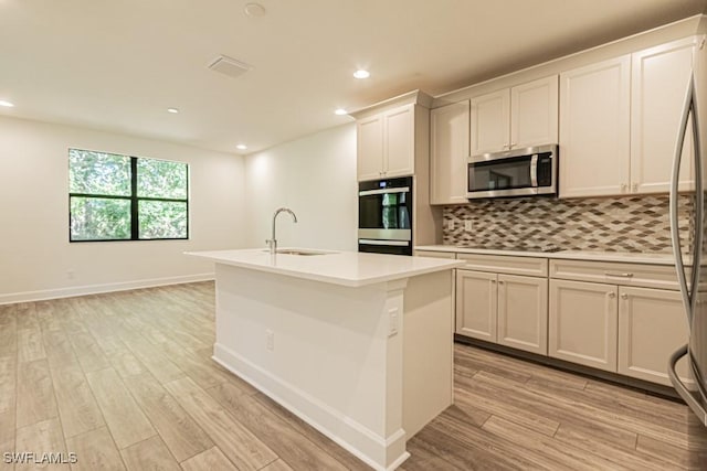 kitchen with white cabinets, sink, an island with sink, light hardwood / wood-style floors, and stainless steel appliances