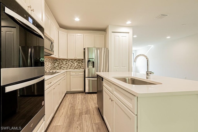 kitchen with white cabinets, a center island with sink, stainless steel appliances, and light hardwood / wood-style floors