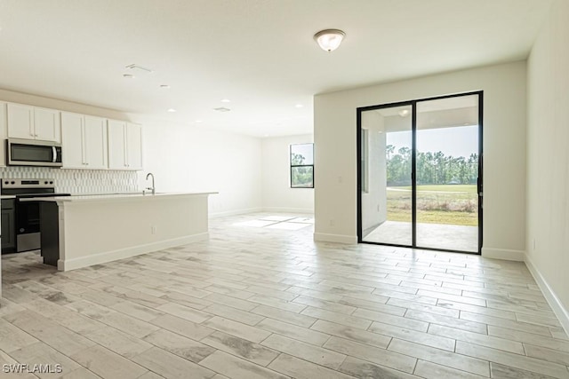 kitchen featuring a kitchen island with sink, white cabinets, light hardwood / wood-style flooring, decorative backsplash, and stainless steel appliances