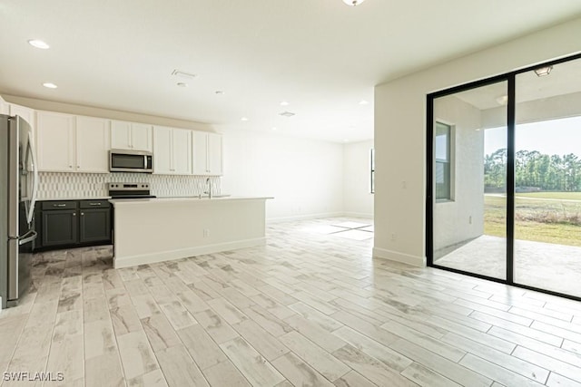 kitchen featuring white cabinets, a center island with sink, decorative backsplash, light wood-type flooring, and appliances with stainless steel finishes