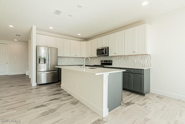 kitchen with stainless steel appliances, light hardwood / wood-style floors, gray cabinetry, and an island with sink