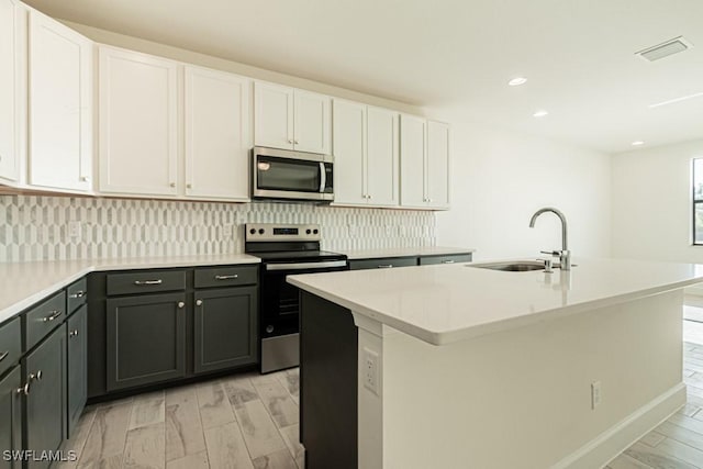 kitchen with stainless steel appliances, white cabinetry, and a center island with sink