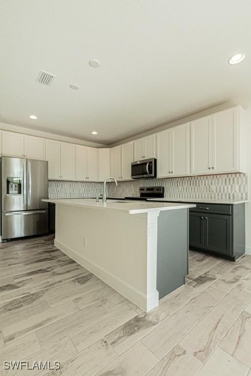 kitchen with white cabinetry, an island with sink, appliances with stainless steel finishes, and light hardwood / wood-style flooring