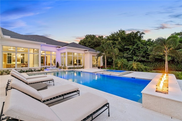 pool at dusk featuring a patio area, an in ground hot tub, and a fire pit