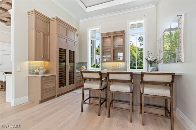 bar featuring light stone countertops, tasteful backsplash, ornamental molding, light hardwood / wood-style flooring, and wine cooler