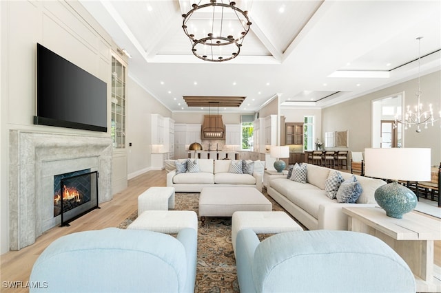 living room featuring a notable chandelier, a raised ceiling, light wood-type flooring, and a premium fireplace