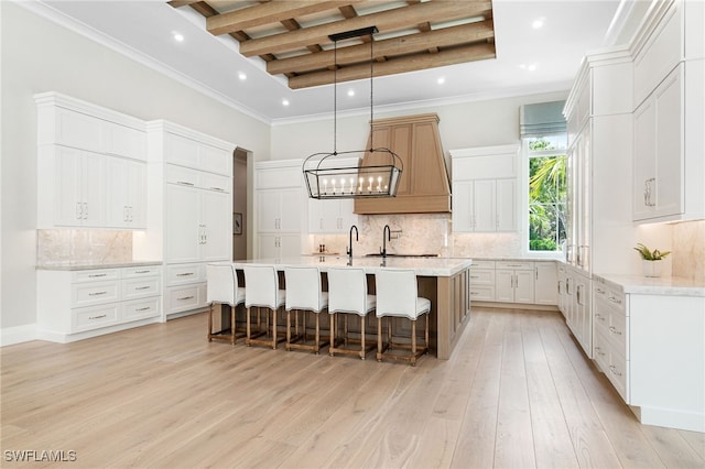 kitchen featuring beamed ceiling, a large island with sink, light hardwood / wood-style floors, decorative backsplash, and white cabinets