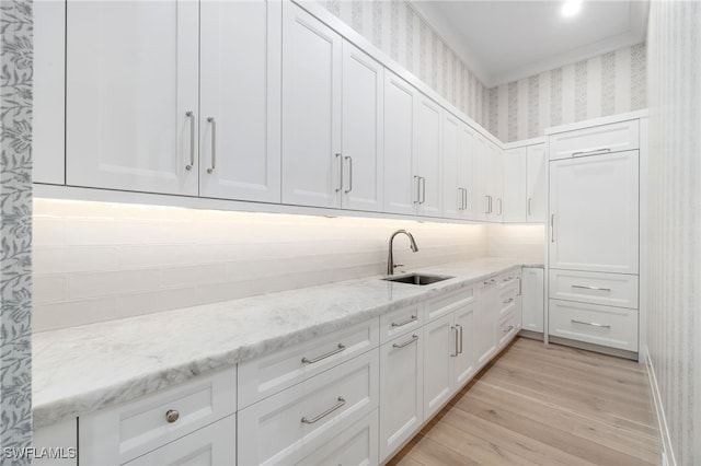 kitchen with white cabinets, light stone counters, light hardwood / wood-style flooring, and sink