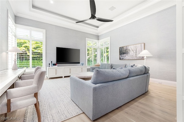 living room featuring ceiling fan, a tray ceiling, a wealth of natural light, and light hardwood / wood-style flooring