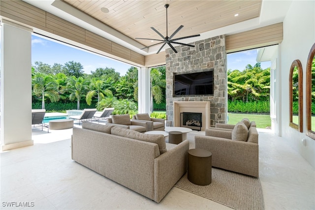 living room with an outdoor stone fireplace, ceiling fan, wood ceiling, and a wealth of natural light