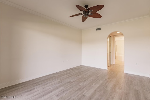 empty room with arched walkways, light wood-style flooring, ornamental molding, ceiling fan, and baseboards