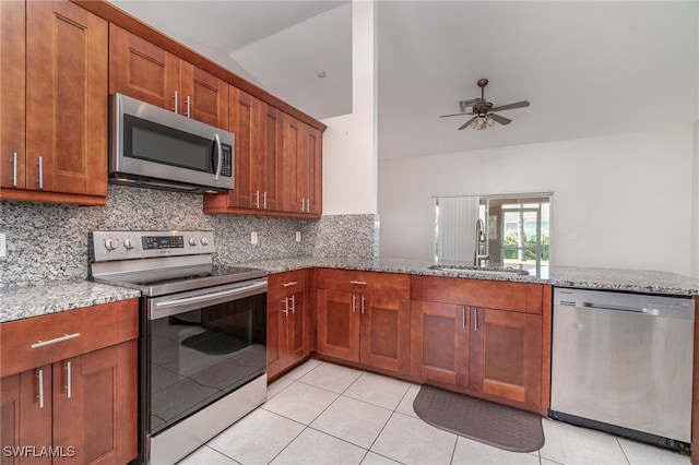 kitchen featuring vaulted ceiling, light tile patterned floors, appliances with stainless steel finishes, tasteful backsplash, and light stone counters