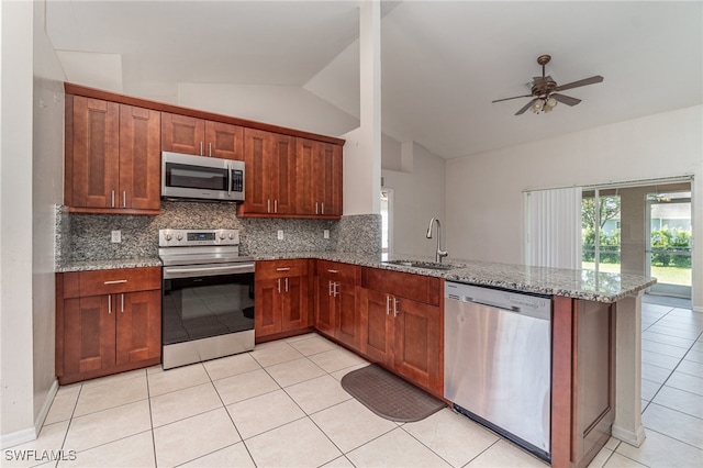 kitchen featuring kitchen peninsula, light stone counters, stainless steel appliances, vaulted ceiling, and sink