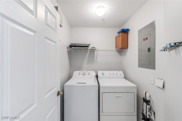 clothes washing area with a textured ceiling, electric panel, and washer and clothes dryer