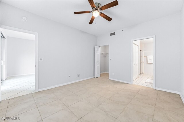 unfurnished bedroom with light tile patterned floors, a closet, ceiling fan, a walk in closet, and ensuite bath