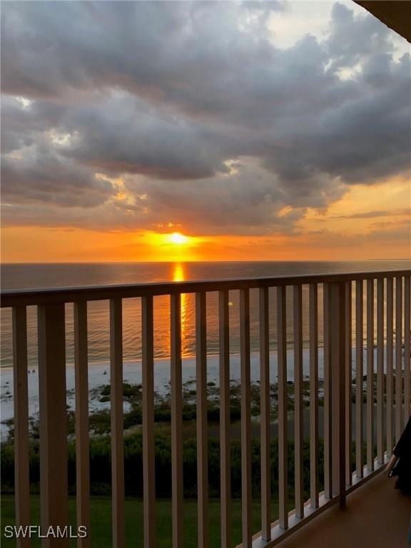 balcony at dusk featuring a water view and a view of the beach