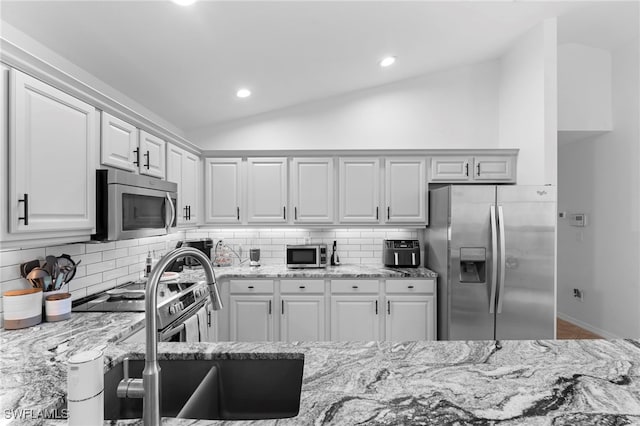 kitchen with stainless steel appliances, lofted ceiling, white cabinetry, and tasteful backsplash